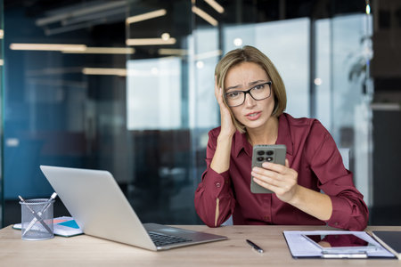 Businesswoman feeling stressed and overwhelmed. Holding a mobile phone with a worried expression....