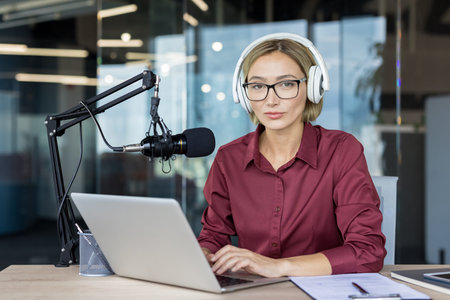 Woman wearing headphones and glasses, looking at the viewer while recording a podcast in a modern...