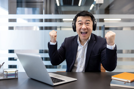 Asian man in a suit celebrating a successful business outcome or personal achievement, wearing...