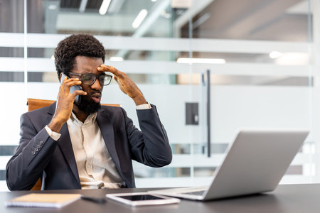 Young businessman experiencing a severe headache and corporate pressure while actively speaking on a...