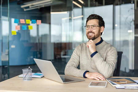 Businessman sitting at his desk, smiling and contemplating new ideas while working in a modern...