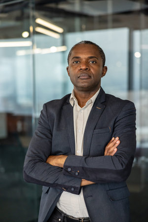 Experienced professional man standing with arms crossed, conveying confidence and authority in a modern office environment, symbolizing leadership and success in businessの写真素材