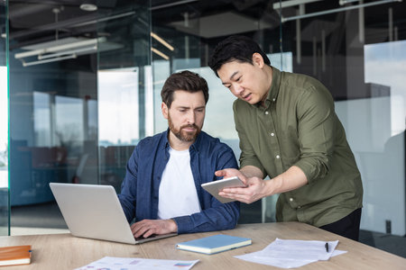 Business colleagues working together in a modern office, one typing on a laptop while the other is...