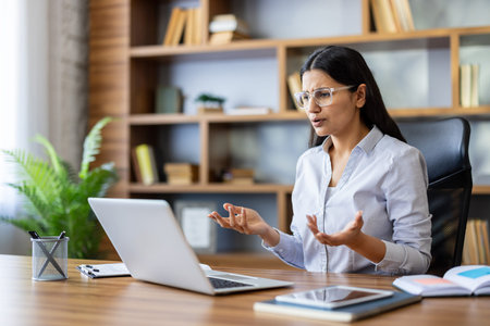 Businesswoman looking confused and gesturing during a video conference on laptop, frustrated by a...