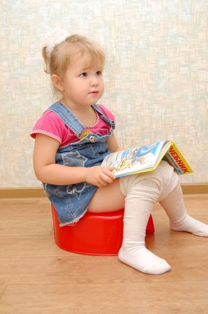 Little girl sitting on red potty with open bookの写真素材