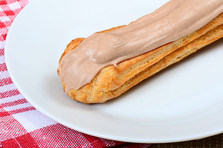 Eclair with a cream on a plate close up
