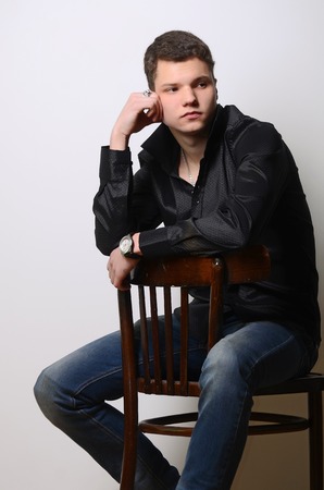 Fashion portrait of young cute man in black shirt poses over wallの写真素材
