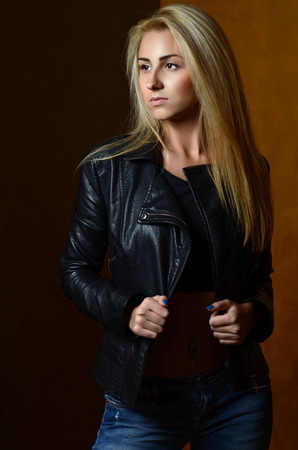 Sexy blonde model wearing leather jacket and jeans posing fashion in the studioの写真素材