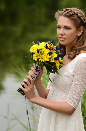 Beautiful natural young blonde smiling woman on field keep in hand yellow flowersの写真素材
