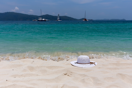A white female hat lies on the sand on the seashore. Beautiful view of the seascape with the ships on the horizon. Island Coral.の写真素材