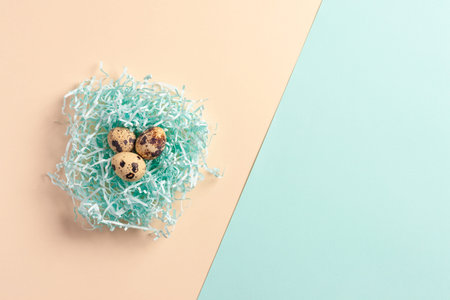 Easter composition made of quail eggs in a nest on a background of mint and beige paper.
