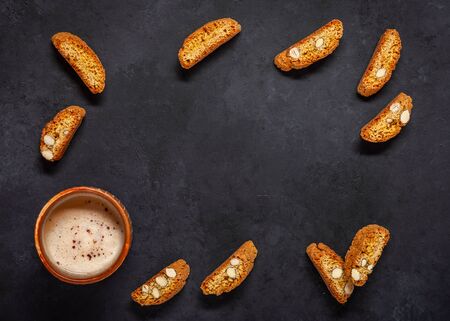 Biscotti on a black background. Frame made of a cup of cappuccino and cookies with almonds. Top view. Copy space.の写真素材
