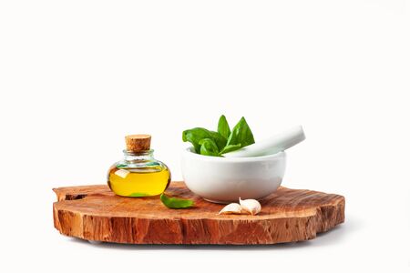 Basil leaves in a mortar, garlic and olive oil on a wooden cutting board. White background. Isolated.の写真素材