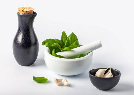 Basil leaves in a mortar, garlic and olive oil on a white backgroundの写真素材