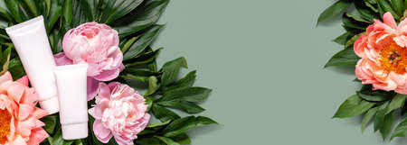 Flat lay composition with cosmetic products and peony flowers on a green background. Web banner. Copy space. Top viewの写真素材