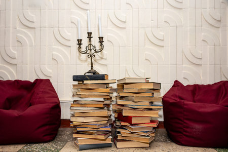 A vintage candlestick on a tall pile of books between red beanbag chairs.の写真素材