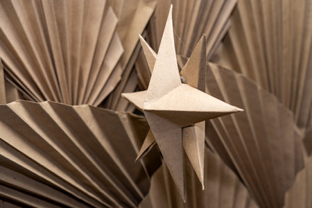 A charming paper star ornament is suspended against a backdrop of intricately folded brown paper. The unique texture and shapes create a captivating visual display, ideal for festive occasions.の写真素材