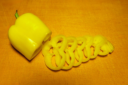 A yellow bell pepper is sliced into spiral-shaped ribbons, lying on a warm, textured surface. The vibrant color adds a cheerful touch to the kitchen setting.の写真素材