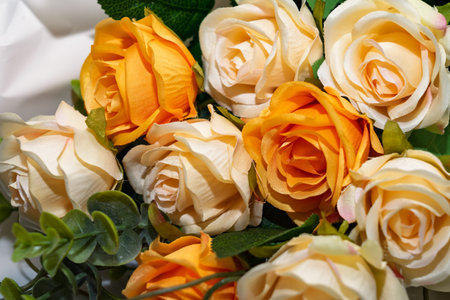 A vibrant bunch of artificial roses features shades of yellow and cream, arranged beautifully among greenery. Perfect for enhancing any decorative space or occasion.の写真素材