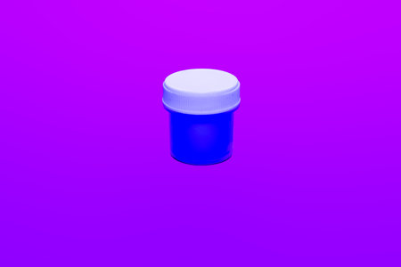 A small blue container sits centrally against a bold purple background, creating a striking visual effect. The container has a white lid and appears to be well-lit, emphasizing its color.の写真素材