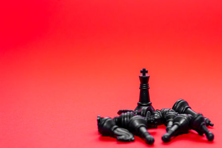 A black king stands tall among fallen black chess pieces on a bright red surface. This striking contrast highlights the dramatic outcome of the game, emphasizing defeat.の写真素材