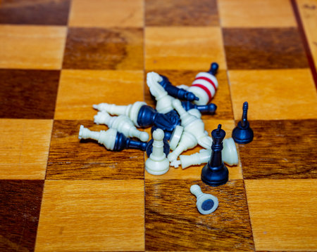 A collection of chess pieces lies in disarray on a wooden chessboard, indicating a heated game. Some pieces are toppled over, creating a dramatic effect in the setting.の写真素材