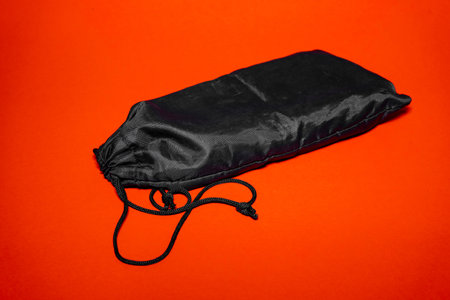 A black drawstring pouch is positioned against a bold orange backdrop. The pouch is neatly closed, showing its smooth texture and practical design, ideal for storage.の写真素材