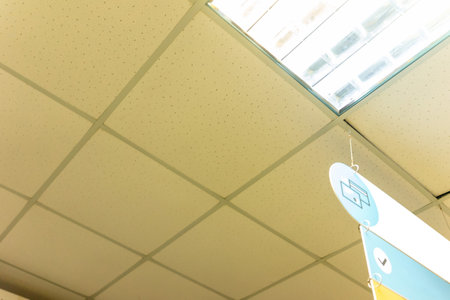 The ceiling features grid tiles with a skylight allowing natural light. A colorful sign hangs down, likely indicating information relevant to the workspace below.の写真素材