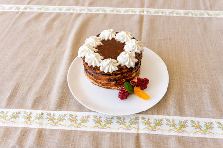 A beautifully crafted layered cake sits on a white plate. Topped with dollops of whipped cream and...