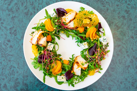 A creative salad presentation with arugula, roasted squash, and grilled chicken, garnished with edible flowers and cheese, highlighting seasonal flavors in an elegant circular design.の写真素材