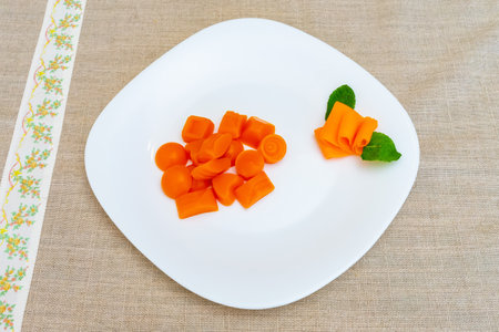 An assortment of creatively shaped carrot slices rests on a white plate. The vibrant orange pieces include small circles and decorative ribbons, accompanied by fresh mint leaves.の写真素材