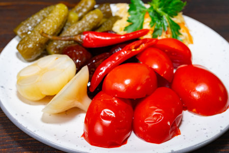 A vibrant platter features pickled tomatoes, cucumbers, and peppers, garnished with fresh herbs. This dish showcases a variety of textures and flavors ideal for appetizers.の写真素材
