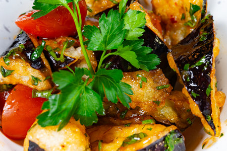 A colorful dish featuring crispy fried eggplant slices garnished with fresh parsley and ripe tomatoes. The meal showcases vibrant colors and a delightful presentation, perfect for sharing.の写真素材