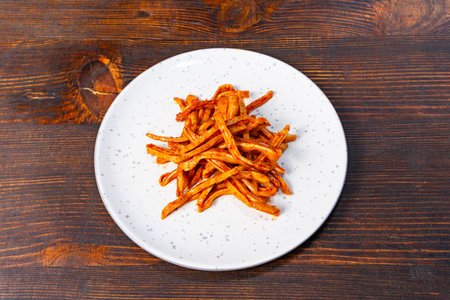 A generously serving of crispy sweet potato fries is neatly arranged on a white plate. The fries...