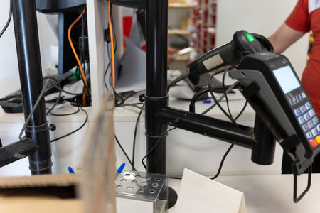A retail worker stands at the checkout counter, using a scanner to process items. Payment systems...