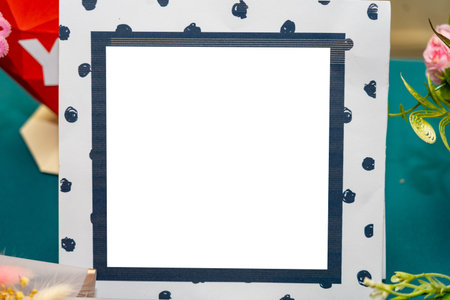 A blank frame with a navy blue polka dot design sits on a colorful table. The setting includes...