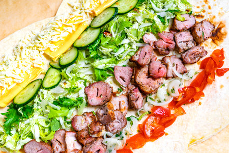 A large tortilla is filled with marinated pork, fresh cucumbers, lettuce, tomatoes, onions, and shredded cheese.の写真素材