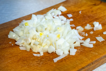 Fresh onions are finely chopped on a wooden cutting board in a modern kitchen. The crisp white pieces showcase the preparation for a delicious meal.の写真素材