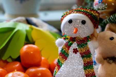 A cheerful snowman made of sparkly materials stands among vibrant fruits, including orange tangerines and green leaves, creating a joyful holiday atmosphere in a cozy setting.の写真素材