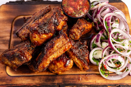 Grilled ribs are arranged attractively on a wooden platter, paired with a vibrant salad of onions, cucumbers, and herbs, along with a small bowl of salsa for dipping.の写真素材