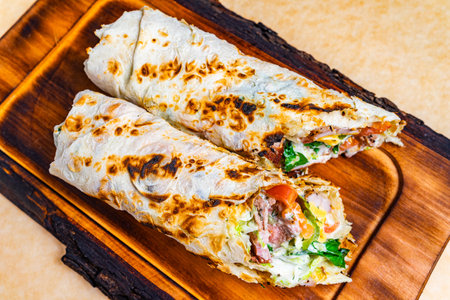 Two flavorful wraps are placed on a rustic wooden board, showing fresh vegetables, meats, and sauces.の写真素材