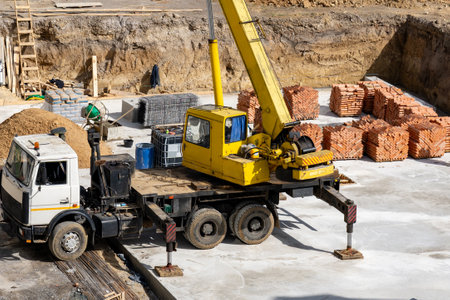 A busy construction site features a yellow crane lifting building materials. Piles of bricks and supplies are neatly arranged around the work area, indicating active development in progress.の写真素材