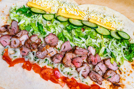 A large wrap is filled with grilled meat, fresh greens, tomatoes, cucumbers, and cheese. The wrap is displayed on a wooden surface, highlighting colorful ingredients.の写真素材