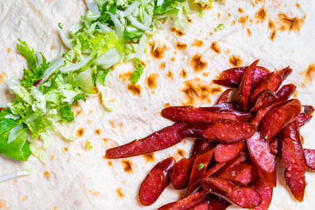 Sliced sausage is arranged neatly beside fresh lettuce on a flatbread. The vibrant colors and textures create an appealing layout, perfect for a tasty meal or snack.の写真素材