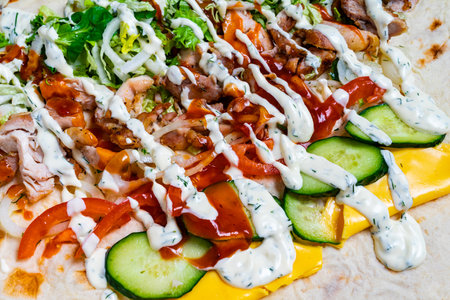 A vibrant wrap features an array of fresh ingredients, including lettuce, tomatoes, cucumbers, shredded meat, and drizzled sauces. The colorful display highlights a perfect meal choice.の写真素材