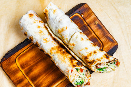 Two grilled wraps with a golden-brown crust rest on a wooden board, showing a mix of fresh...