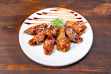 Delicious glazed chicken wings served on a white plate with sesame seeds and sauce decorationの写真素材