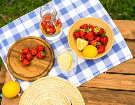 A cheerful outdoor picnic showcases vibrant strawberries displayed in bowls alongside refreshing lemonade.の素材