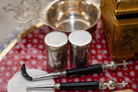 Close-up image of metal liturgical vessels and tools used in Christian religious ceremonies. The composition includes two silver containers, a small metal bowl, and two ritual instruments with black handles and crossesの写真素材