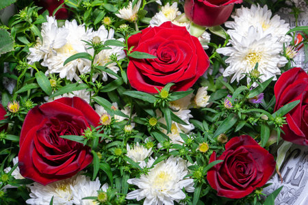 A vibrant arrangement of red roses and white daisies fills the frame. Their colors contrast beautifully, creating a cheerful display perfect for a celebration or special occasion. The greenery adds freshness to the composition.の写真素材
